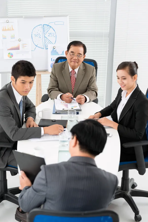 会議室でグラフを背景にチームミーティングを行うビジネスパーソン